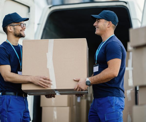 Happy manual worker cooperating while carrying cardboard boxes in a delivery van.